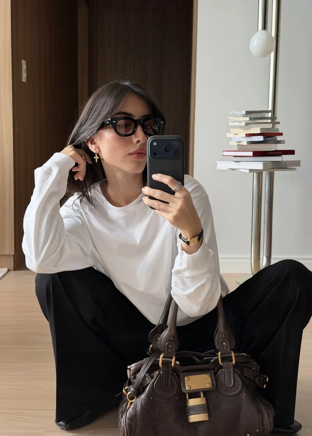 Maju tirando uma selfie no espelho, sentada no chão com uma bolsa marrom