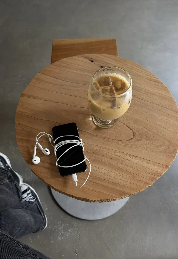 Café gelado em uma mesa de madeira, com celular e fones de ouvido